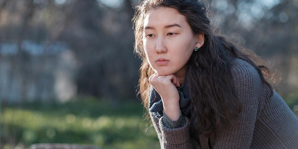 Asian woman in a park, deep in thought, emotional, depressed